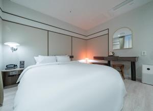 Un dormitorio con una gran cama blanca y un escritorio. en 호텔 레이블 안산, en Chungang-yŏk