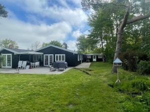 a black house with a patio and a yard at Summerhouse Denmark in Tisvildeleje 700 m walk from beach in Tisvilde