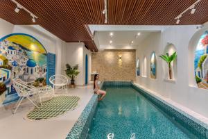 Una mujer se sienta en el borde de una piscina en una casa. en LG Villa My Khe Beach, en Da Nang