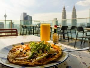 a pizza on a plate on a table with a glass of orange juice at Imperial Luxury Suites KLCC by Moonway in Kuala Lumpur