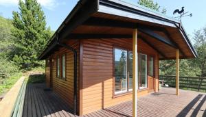een houten hut met een groot raam op een terras bij Cosy Cabin Escape with Hot Tub & Lake View in Lundur
