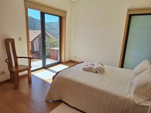 ein Schlafzimmer mit einem Bett und einem Stuhl und einem großen Fenster in der Unterkunft Casa Vilarinha Gerês in Taboabela
