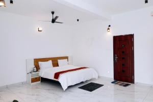 a white bedroom with a bed and a red door at Dreams Holidays Vagamon in Vagamon