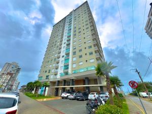 a large building with cars parked in a parking lot at Apto em condomínio Pé na areia 3 Quartos Cozinha Completa Sacada com Churrasqueira Vaga de Garagem Piscina borda infinita Academia Quadra de esportes Sala de Jogos Summer Home Club acesso direto a praia in Piçarras