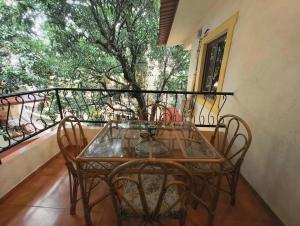a glass table and chairs on a balcony with a tree at Navilehomestay in Candolim