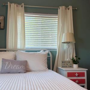 a bed with white pillows and a window with a window blind at Cozy Coastal Cottages of Dunedin 1 in Dunedin