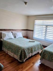 Un dormitorio con una cama con una manta verde y una ventana. en Hostal Punto Austral, en Puerto Montt