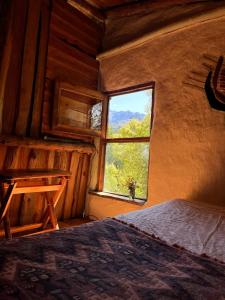 a bedroom with a bed and a window in a cabin at Cabaña de barro con Bosque, rio, arte y apicultura in Epuyén