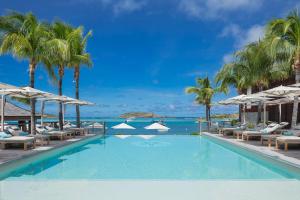 a swimming pool with chairs and palm trees and the ocean at Le Barthélemy Hotel & Spa in Gustavia
