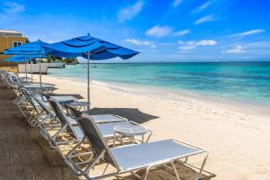 une rangée de chaises et de parasols sur une plage dans l'établissement Laguna Del Mar #19 - Seven Mile Beach, à Dog City