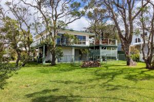 a white house with a balcony and trees at Ocean Echoes - Pet Friendly with Ocean Glimpses in Culburra Beach