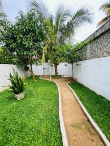 a garden with a white wall and trees and a path at Samara Beach Stay in Weligama +17 photos