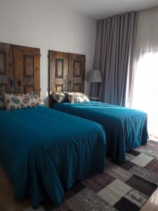 Duas camas num quarto com lençóis azuis e uma janela. em DH Country House em Évora