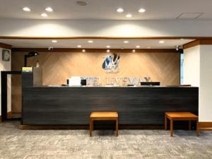 a lobby with a reception desk with two benches and avertisement at HOTEL LiVEMAX Toyooka in Toyooka