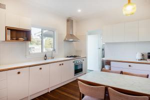 モリーモックにあるThe Blue Beach House - Pet Friendly Coastal Escape in Mollymookの白いキャビネットとテーブルと椅子のあるキッチン