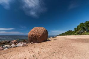a large rock sitting on a beach near the water at Lauču Akmens in Skulte