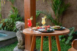 a table with two plates of food and two drinks at Seelong Villa Ubud by Dhananjaya Hospitality in Tampaksiring