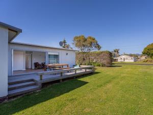 une maison avec une terrasse en bois à côté d'une cour dans l'établissement Caddy's Shack - Whangamata Holiday Home, à Hauturu