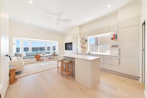 a kitchen with white cabinets and a living room at Beachfront 1 Bed across from iconic BONDI BEACH in Sydney