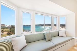 a couch in a room with windows and a beach at Beachfront 1 Bed across from iconic BONDI BEACH in Sydney