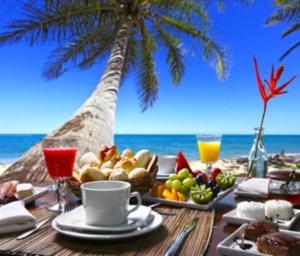 a table with a breakfast on the beach with a palm tree at L'Oasis de L'Anse Bleue in Le Diamant