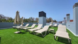 een rij ligstoelen en een parasol op een gazon bij Sunset Arguineguin by CanariasGetway in Arguineguín