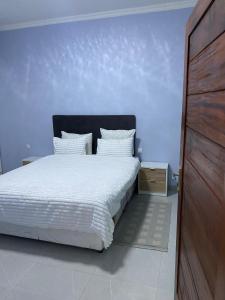 a bedroom with a white bed with a blue wall at Villa Djonasse, a Residence of Exellency in Fombeni