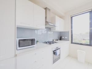a white kitchen with a microwave and a window at Mt Waverley Spacious 2br2ba Parking Wifi Balcony in Mount Waverley