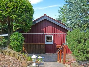 a red shed with a fence and trees at Holiday Home Zedernhütte by Interhome in Bremke