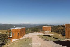 two wooden buildings on a hill with a dirt road at Cabana com vista panorâmica e jacuzzi VST022 in São Paulo dos Pinhais