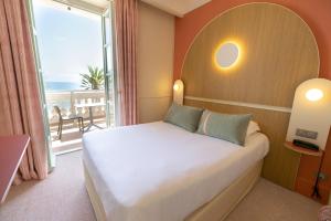 a bedroom with a bed and a large window at Hôtel Vacances Bleues Balmoral in Menton