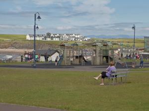 une femme assise sur un banc près d'une aire de jeux dans l'établissement Holiday Home Seacrest - TR4 HH No 6 - 3 Bed by Interhome, à Bundoran 17 autres photos