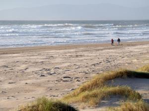 2 personnes marchant sur une plage près de l'océan dans l'établissement Holiday Home Seacrest - TR4 HH No 6 - 3 Bed by Interhome, à Bundoran