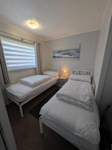 two twin beds in a room with a window at Beachcomber, Two bed Chalet on Sunbeach Holiday Park - Sleeps 4, pet friendly, FREE pool and entertainment passes included - plus WiFi - only 300m from the beach! in Scratby +19 photos