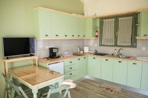 eine Küche mit grünen Schränken, einem Tisch und einem TV in der Unterkunft Olive Coast Houses in Kyparissia