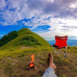 a person laying next to a chair and a fire at narangala skycamping 