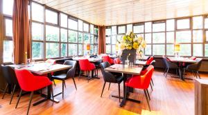 a restaurant with tables and red chairs and windows at Bastion Hotel Bussum Hilversum in Bussum