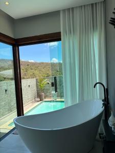 a bath tub in a bathroom with a view of a pool at Cipó Lofts - Serra do Cipó in Santana do Riacho