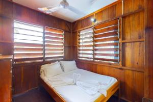 a small bed in a room with wooden walls and windows at Bonefish at Carol's Cabanas -Gold Standard Certified in Placencia Village