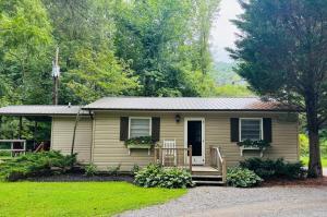 a small yellow house with a porch and a yard at Cozy Creek Cottages in Maggie Valley