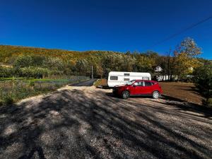 une voiture rouge garée sur le bord de la route avec une remorque dans l'établissement Camping Kosovo Treehouse campground of anykind, à Ferizaj