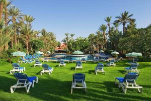 een groep stoelen en parasols op het gras bij een zwembad bij Hôtel Marrakech Le Semiramis in Marrakesh