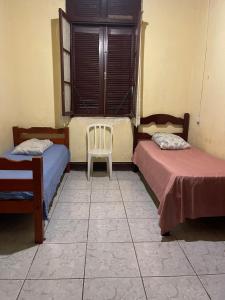 a room with two beds and a chair and a window at HOTEL PENSÃO COLONIAL - Centro Atibaia in Atibaia