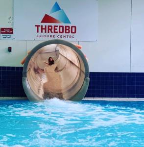 une personne utilisant un toboggan aquatique dans une piscine dans l'établissement PISTE LUXURY CHALET - THE GRANDE - Oaks Lake Crackenback Resort, à Crackenback