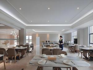 PuyuanにあるVienna Hotel Zhejiang Tongxiang Puyuanのテーブルと椅子が備わる部屋に立つ女性