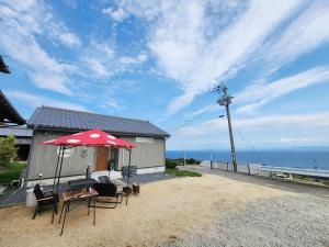 a table and chairs with an umbrella in front of a house at 「淡路島一棟貸宿　野うさぎ 」高台から海を望む貸別荘！2023年新築離れの素泊まり in Noda