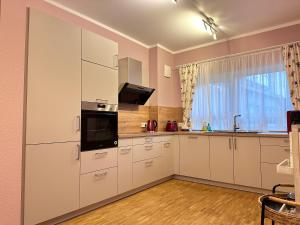 une cuisine avec des armoires blanches, un évier et une fenêtre dans l'établissement Ferienwohnung Seeperle, à Bad Zwischenahn