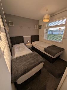 a bedroom with two beds and a window at Lazy Dayz, Chalet 179, Hemsby - Two bed chalet, sleeps 4, pet free, close to beach in Hemsby