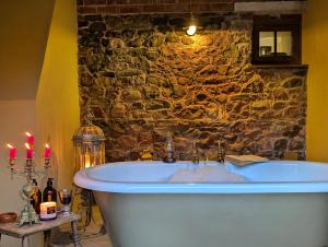 une baignoire dans une pièce avec un mur en pierre dans l'établissement Romantic Country Cottage with log burner, garden patio, outdoor tub and country views- Brecon Beacons National Park, à Llangadog 25 autres photos
