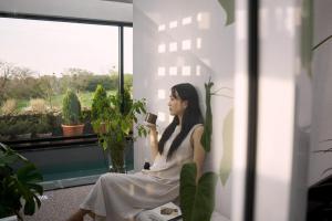 une femme assise sur un rebord de fenêtre tenant un téléphone portable dans l'établissement Jeju Rapauza Stay, à Yusuam
